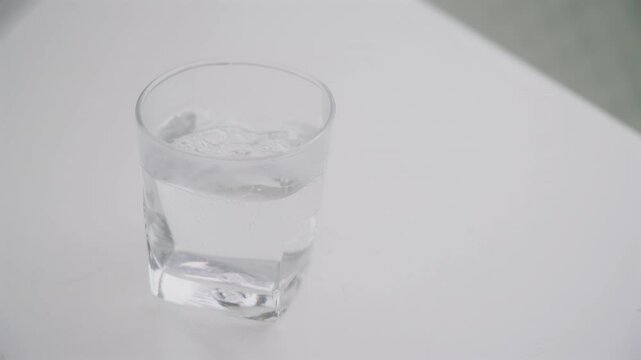A glass placed on a white table being poured with water, top view angle