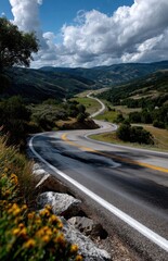 Winding mountain road leading through a valley under cloudy sky