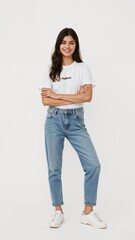 Full length of confident Pakistani teenage girl smiling in a casual outfit in a white tshirt and jeans standing with her arm and leg crossed on plain white background