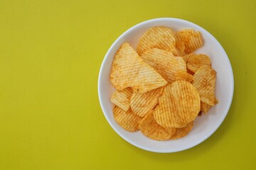 Potato chips in white plate on yellow background
