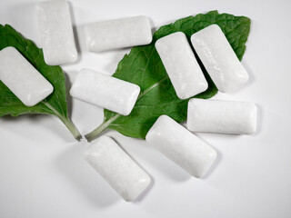 Isolated mint chewing gums on a white background next to a spearmint leaf,