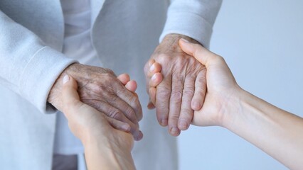 Young woman's hands gently holding the hands of an elderly person, offering comfort, support, and...