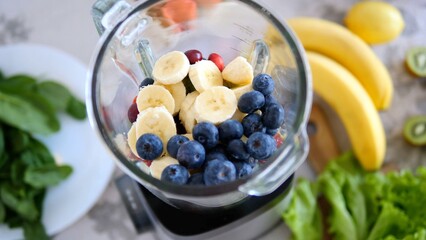 Sliced bananas, blueberries, and cranberries are inside a blender jar, ready to be blended into a...