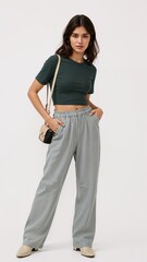 Full length of confident Mexican woman in a tuckedin tee and wideleg pants with one hand holding a phone at her side on plain white background