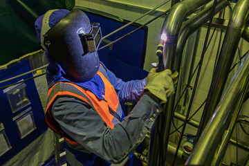 Male worker wearing protective clothing of repair pipe stainless argon welding industrial
