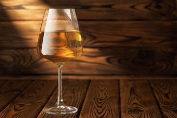 Glass white wine basks in dramatic beam of light, sitting elegantly on rustic wooden table