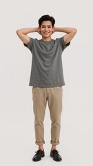 Full length of confident Singaporean man in a casual tee and rolledup chinos standing with hands behind his head and grinning on plain white background