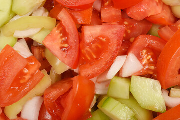 A close-up of the texture of a freshly chopped tomato, cucumber, bell pepper, and onion salad