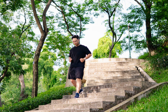 Man in black workout clothes descends stone stairs in a lush park during a sunny morning