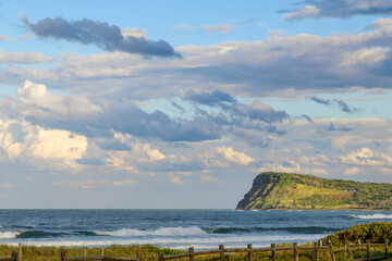 A scenic view of the rugged coastline and sunlight on the rugged green headland under a dramatic,...