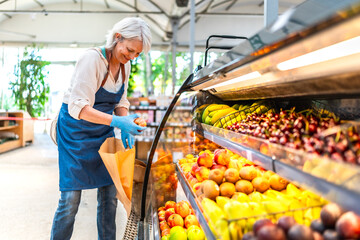 Senior saleswoman arranging fresh fruits in supermarket display case