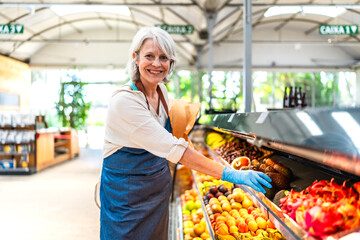 Senior saleswoman arranging fruits on display in supermarket