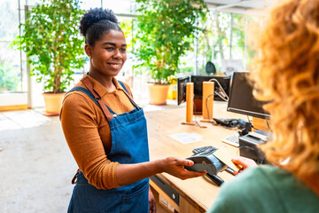 Shop assistant accepting contactless payment from customer in plant store