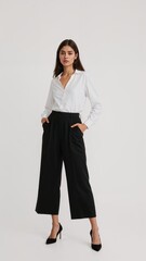 Full length of confident Italian woman in a professional white blouse and black culottes standing with one arm on waist and other holding phone on plain white background