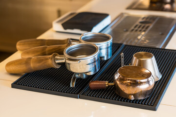 Coffee shop counter with wooden-handled portafilters, copper milk jug, and tamper showcased on a...