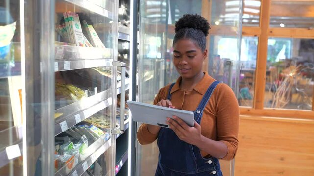 Professional female retail worker scanning inventory using digital tablet while standing near refrigerated shelves in modern grocery store interior - Powered by Adobe