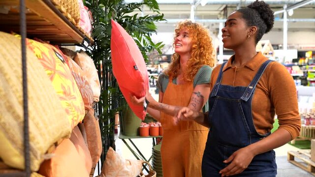 Saleswomen presenting and comparing soft, colorful decorative pillows while assisting customers in modern furniture retail environment
