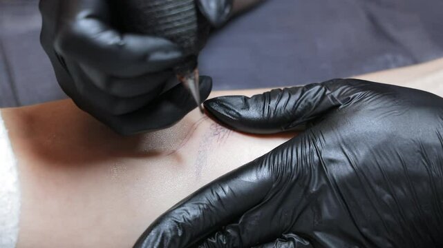 Close-up of tattoo artist working on skin. Tattoo artist wearing black gloves uses a tattoo machine to create a detailed design on a client's forearm in studio.