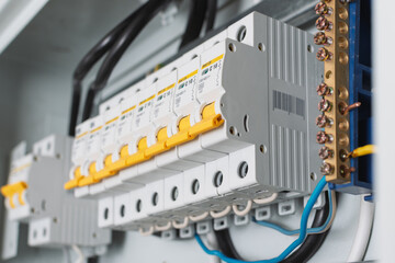 Close-up view of circuit breakers with yellow levers in a distribution panel highlights precision wiring, copper busbar, and technical details of home electrical installation.