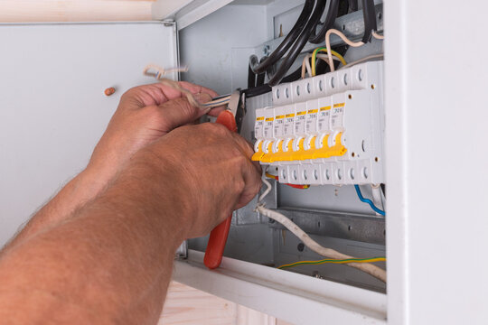 Electrician uses side cutters to trim and organize wires inside the fuse box, ensuring safety and professional wiring installation.