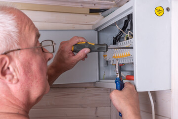 Skilled electrician in glasses uses screwdriver and pliers for precise adjustment of electrical...