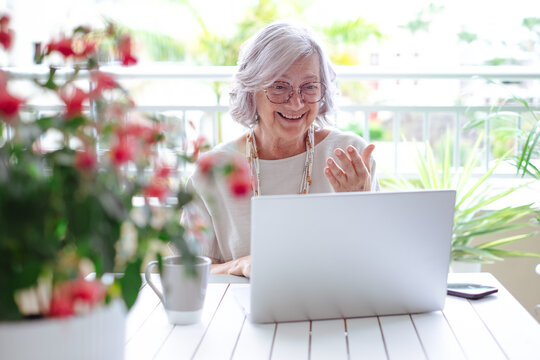 Video call concept. Smiling gray haired senior woman working on laptop sitting outdoor on terrace.  Elderly modern lady enjoying tech and social