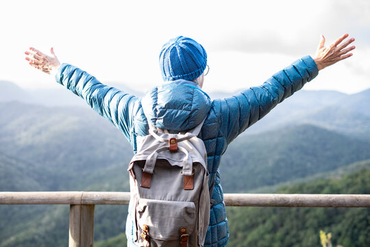 Back view of active senior woman walking outdoors in mountain enjoying freedom and nature looking at scenery landscape. Relaxed elderly woman with backpack live an healthy lifestyle - Powered by Adobe