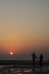 A romantic moment of a young man lifting his partner in his arms while standing in shallow sea water at the beach during sunset
