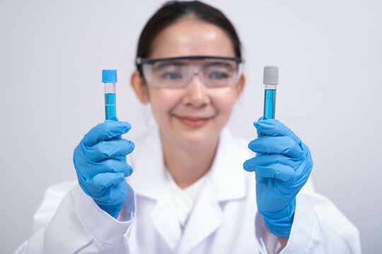 A scientist in a lab coat holds two test tubes, showcasing a cheerful demeanor while demonstrating a scientific process. - Powered by Adobe