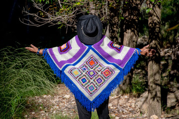 Woman wearing a handmade crochet poncho walking along a path with open arms entering the grotto