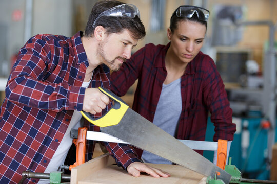 couple carpenter hand sawing wood - Powered by Adobe