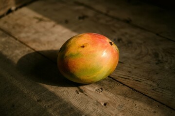 A photograph of a ripe mango resting on a weathered wooden floor