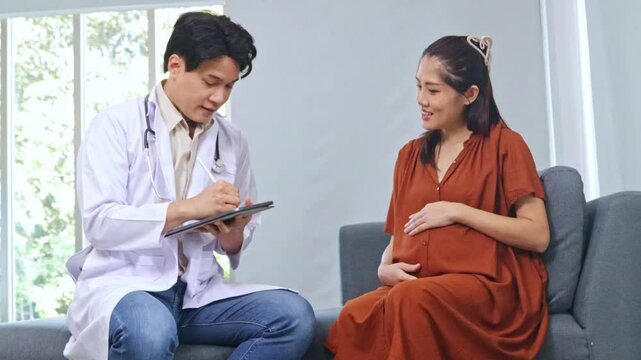 Male obstetrician gynecologist, maternal-fetal medicine specialist examines the health pregnant woman and her nine-month fetus. Sitting and taking notes with interest in order to diagnose symptoms.