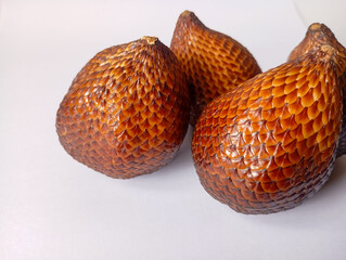 Salak fruit, also known as snake fruit, features its distinctive brown, scaly skin against a plain...