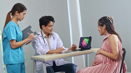 Male obstetrician, gynecologist maternal fetal medicine specialist examines pregnant woman ultrasound results looks at laptop with interest and discusses with female nurse assistant recording results.
