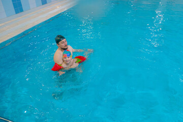 Happy middle-aged father swimming with cute adorable baby in swimming pool. Smiling dad and little child, boy having fun together. Active family spending leisure and time in spa hotel. Concept of kids