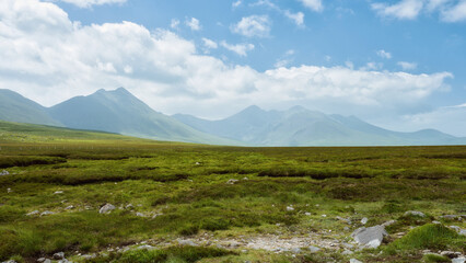 Rolling green hills meet dramatic, dark mountains under a brooding, cloudy sky. A peaceful, yet powerful landscape.