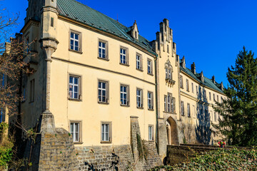 Fototapeta premium Historic gothic revival castle with stone facade and ivy-covered walls under clear blue sky