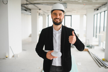 Architect gesturing thumbs up in unfinished building with blueprints