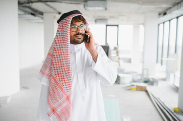 Arab businessman managing investments at construction site during phone call