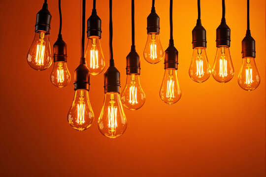 Hanging Edison light bulbs glowing with warm illumination on orange background.