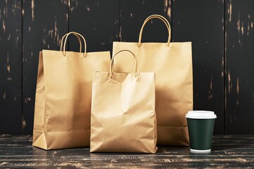 Brown paper bags and coffee cup on wooden surface against dark rustic background.