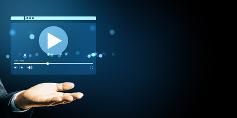 Business hand showing floating video player interface icon on dark blue background with bokeh...