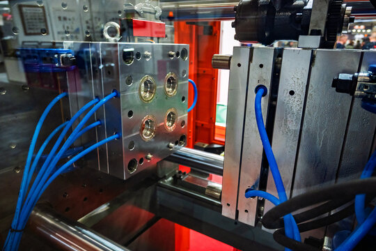 Close-up view of a shiny metal injection molding tool or die with blue hoses, part of an industrial manufacturing machine used for plastic production.