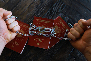Hands in Chains Restricting Movement in Front of Multiple Russian Passports on Dark Wooden Table