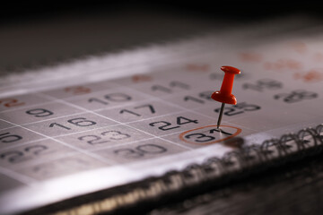 Closeup of Red Push Pin Marking Date on Spiral Bound Calendar for Important Event or Appointment Reminder