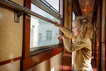 Young girl points excitedly from train window at passing towns