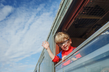 Boy waves cheerfully from green coach window at bustling station