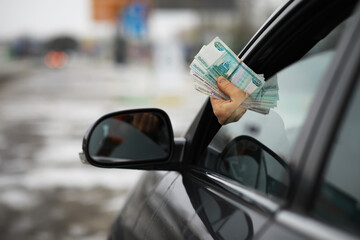 Hand Holding Money Out of Car Window on Blurred Street Background - Financial Transaction or...