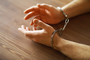 Close-up of Hands in Handcuffs on Wooden Table, Symbolizing Arrest and Justice